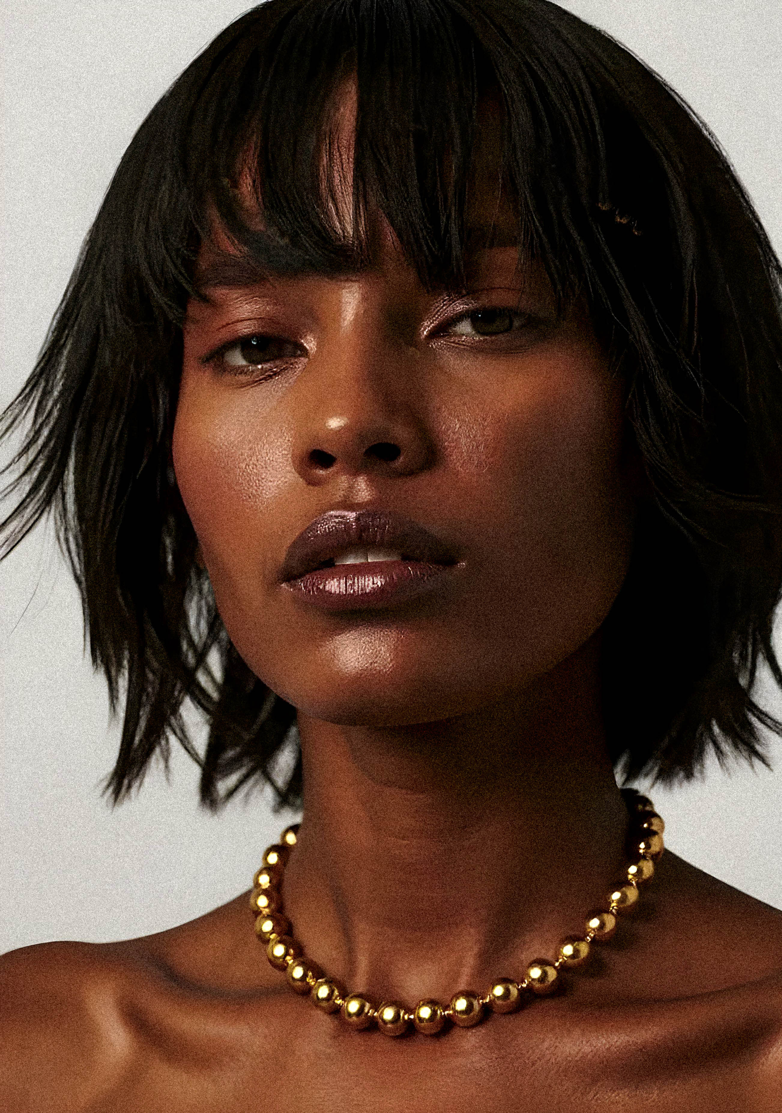 Woman with a short, dark hairstyle wearing a gold necklace against a neutral background