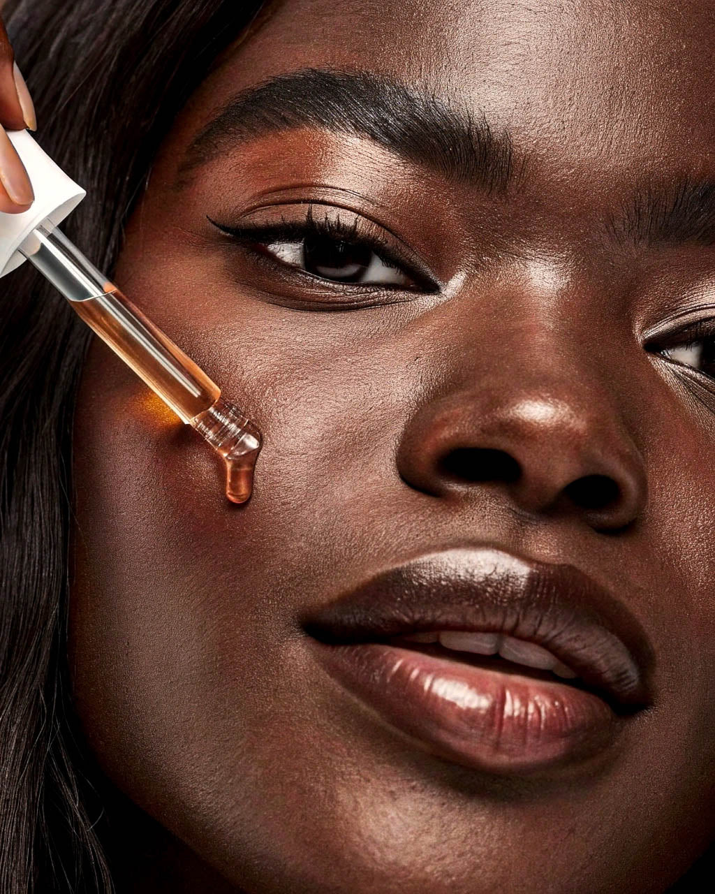 Close-up of a woman applying a dropper of liquid serum to her face.